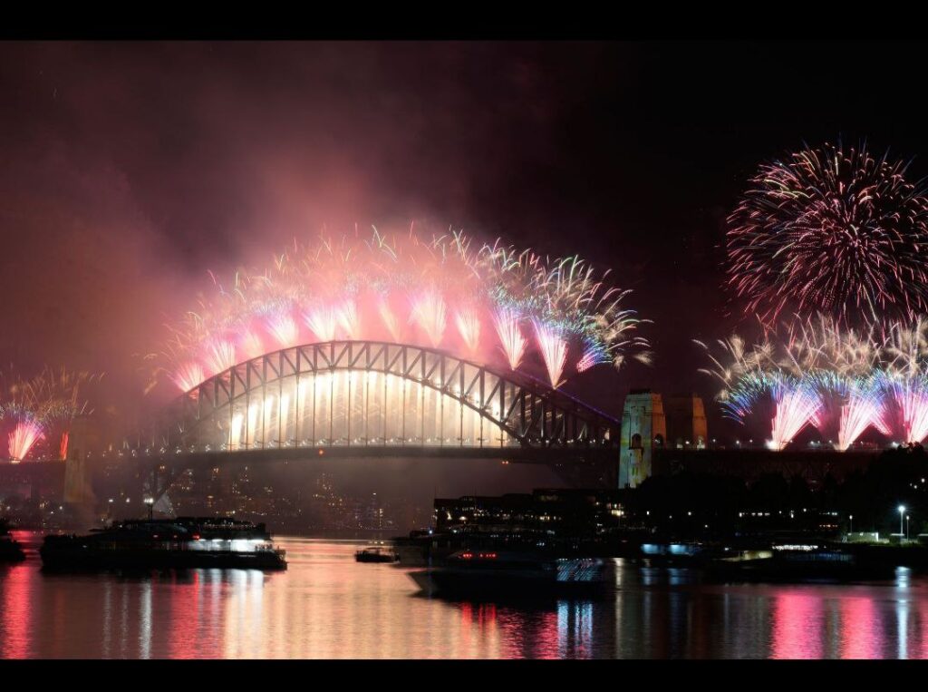 ألعاب نارية حمراء وبيضاء تغطي جسر هاربور ودار أوبرا سيدني في احتفالات رأس السنة.
